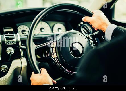 Hands of man wearing suit on steering wheel of luxury car Stock Photo