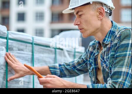 Serious worker in a hardhat touching construction materials Stock Photo
