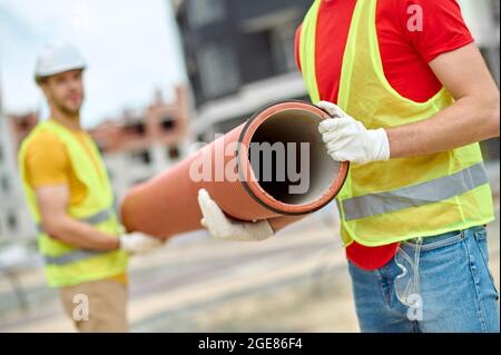 Two workers in cotton gloves holding a corrugated drainage pipe Stock Photo
