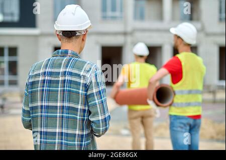 Experienced construction manager in a protective helmet supervising two workers Stock Photo