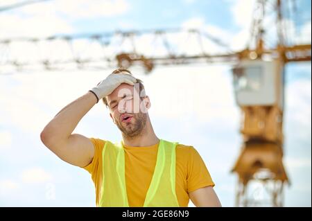 Exhausted builder touching his head with a gloved hand Stock Photo