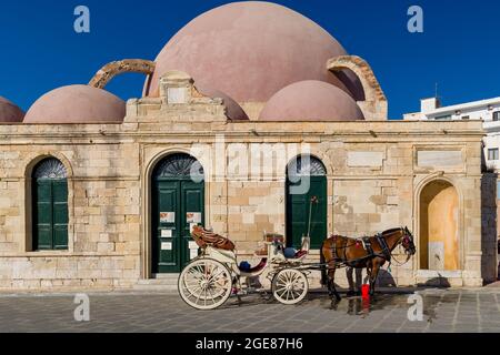 CHANIA, CRETE - 18 JULY 2021: Horses and carriageways await tourists near the ancient mosque on the seafront of Chania, Crete. Stock Photo