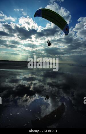 A powered paraglider flying along Coatham Beach with the former Redcar Steelworks in the distance Stock Photo