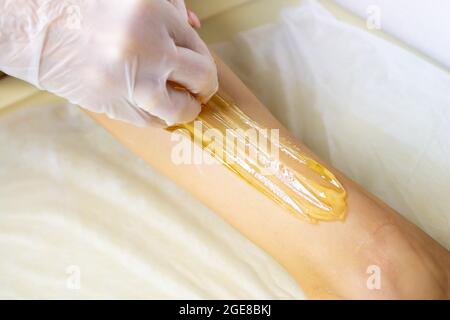 Applying sugar paste to remove hair. The process of removing hair from the legs. The sugaring master applies the paste to the legs. Stock Photo
