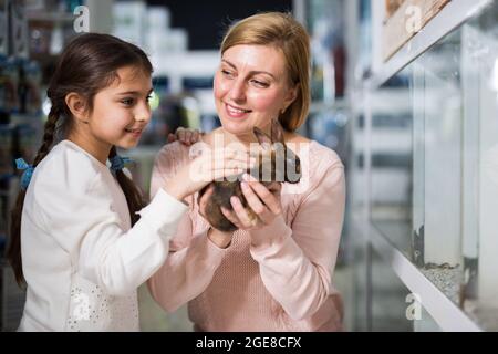 Mother with her daughter holding rabbit together at pet store Stock Photo