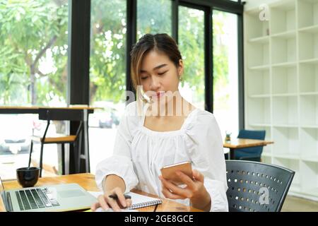 Attractive female freelancer calculating bills and using smartphone for online payment, positive asian woman Stock Photo