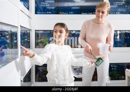 Girl with mother choosing aquarium fish Stock Photo