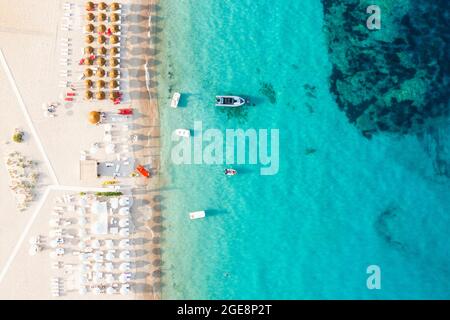 View from above, stunning aerial view of some bathing establishments on a white sand beach bathed by a turquoise water during a beautiful sunset. Stock Photo