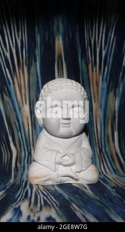 Vertical closeup shot of a meditating Buddha statue made from white gypsum on colorful background Stock Photo