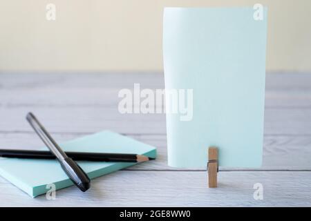 Blank Sticky Note With Laundry Clip Stack Of Colorful Paper Pen Placed On Table. Empty Piece Of Sheet Clipped Beside Pen And Flashy Papers On Desk. Stock Photo