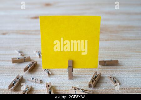 Piece Of Blank Square Note Surrounded By Laundry Clips Showing New Meaning. Empty Sticky Paper Clipped Upright Placed On Top Of Wooden Table Stock Photo