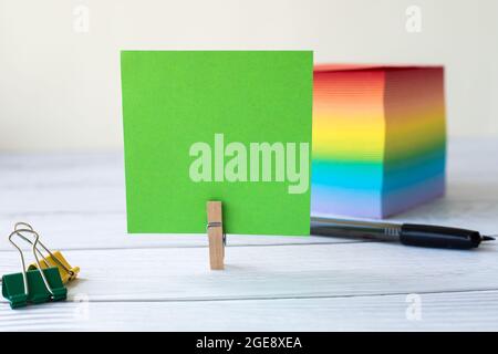 Blank Sticky Note With Laundry Clip Stack Of Colorful Paper Pen Placed On Table. Empty Piece Of Sheet Clipped Beside Pen And Flashy Papers On Desk. Stock Photo