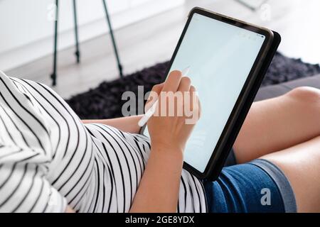 Woman working or drawing on the tablet with pencil and laying on the sofa. A designer or artist works from home Stock Photo