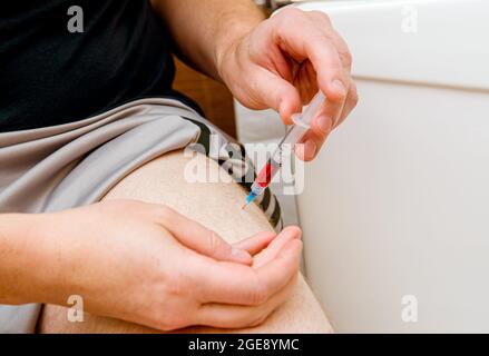 Close up view of man person do the B12 vitamin injection shot in home itself to himself in leg( vastus lateralis muscle) due to B12 deficiency what bo Stock Photo
