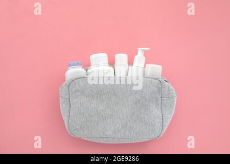 White bottles of cleansing cosmetics in cosmetic bag. Beautiful cosmetic and creams set from cosmetic bag on pink background copyspace. Minimalism cos Stock Photo