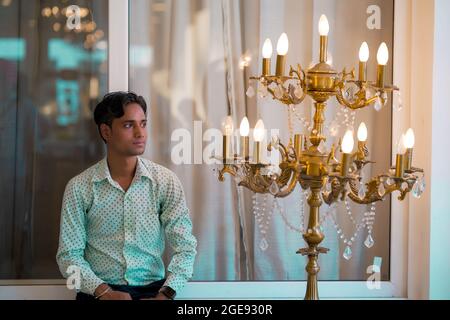 Handsome young Indian man looking off to the side in a patterned dress shirt beside a bright lamp Stock Photo