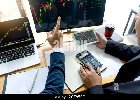 Businessmen are pointing to monitor to view stock market data on desktop computer and discuss it by analysis data from data graph. Stock Photo