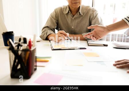 Office atmosphere At the meeting room the staff stands by pointing to the document graph chart on the conference table sepia tone Stock Photo