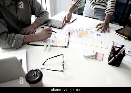 Diverse male mentor and intern talking pointing on paper at work desk teaching how to working with business data on computer internship apprentice men Stock Photo