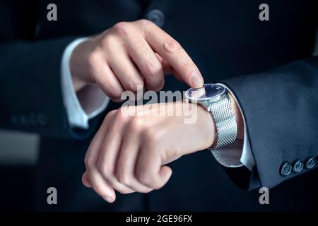 Watch around the wrist of a stylish business man. Busy businessman looking at the time. Stress or hurry at work. Person wearing suit. Stock Photo