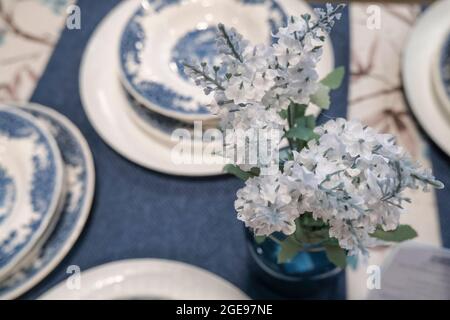 still life table setting. Vase with flowers, candles, blue tablecloth, beautiful plates. Table decor Stock Photo