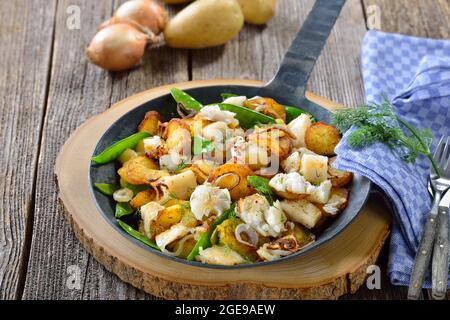 Fried potatoes with pieces of halibut fillet, sugar peas and onion rings, often served in a frying pan Stock Photo