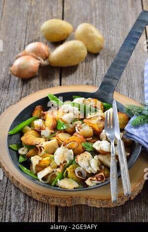 Fried potatoes with pieces of halibut fillet, sugar peas and onion rings, often served in a frying pan Stock Photo