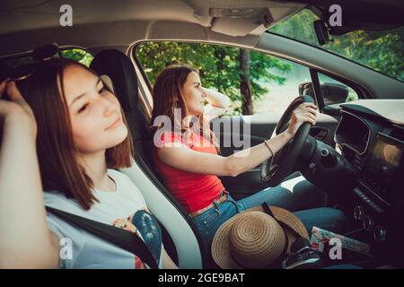 Two young female friends driving in car, enjoy road trip in summer. Stock Photo