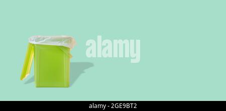 Banner with a green garbage trash bin with bag inside and with its shadow at turquoise solid background with copy space. Concept of waste recycling. Stock Photo