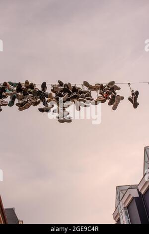 shoes hanging on wires for streetart purpose Norderstrasse in Flensburg. Flensburg, Germany - August 2021 Stock Photo