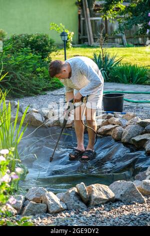 man cleans garden pond bottom with high-pressure washer from mud and sludge. Stock Photo