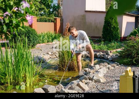 man cleans garden pond bottom with high-pressure washer from mud and sludge. Stock Photo