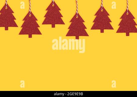 Row of red glittering New Year decorations in a fir-tree shape on a yellow background. Festive concept. Stock Photo
