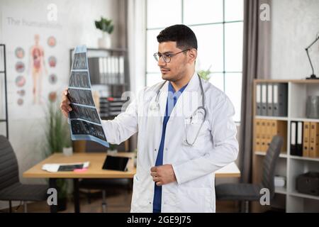 Medical diagnosis concept. Portrait of male Arab doctor oncologist physician examining lungs x-ray computerized tomography scan, working in his office in modern clinic. Side angle view indoor shot. Stock Photo