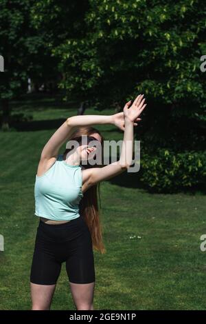 Young caucasian long-haired woman in sportswear is doing yoga in public park. Outdoor workout. Yoga poses Stock Photo