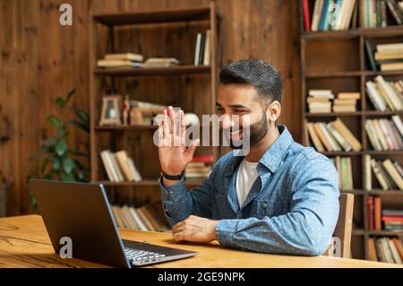 Positive smart indian freelancer guy working on laptop at home office, holding virtual meeting, multiracial eastern male employee using computer app for video call, involved virtual conference Stock Photo