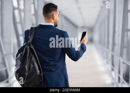 Booking Hotel Online. Arab Man With Backpack Using Blank Smartphone In Airport Stock Photo