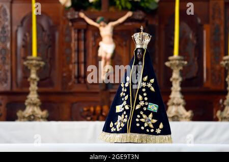 altar with sculpture of Nossa Senhora Aparecida, patron saint of Brazil in selective focus and cross of Jesus Christ in the background Stock Photo