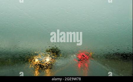 Defocussed traffic viewed through a car windscreen covered in rain,. Focus on raindrops . This is in the fall Stock Photo