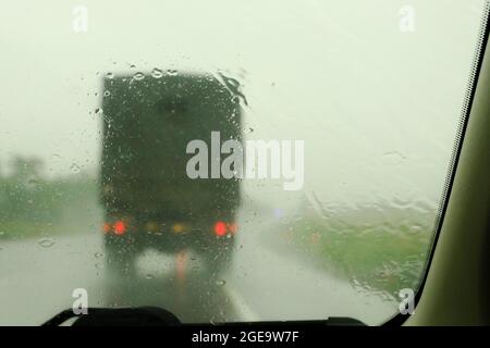 Column of modern military vehicles on the highway. Defocussed traffic viewed through a car windscreen covered in rain. This is in the fall Stock Photo