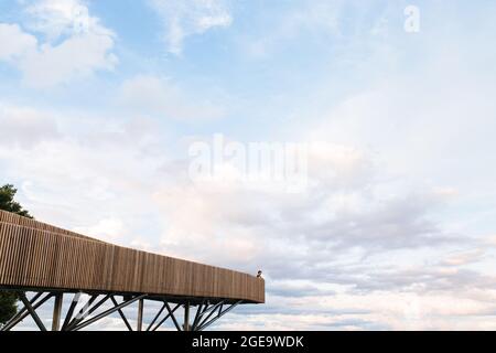 Remote view of person standing on wooden viewpoint on background of amazing sundown cloudy sky Stock Photo