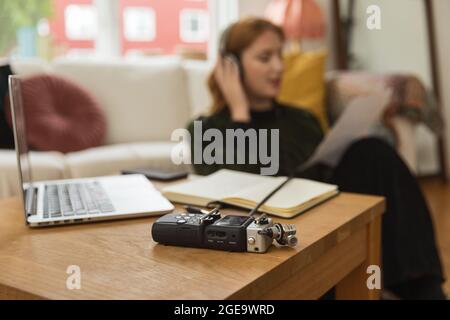 Modern audio recorder placed on wooden table on background of blurred female radio host in headphones recording podcast Stock Photo