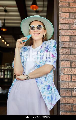 Smiling young female in stylish apparel with cellphone in cafeteria with lamps Stock Photo