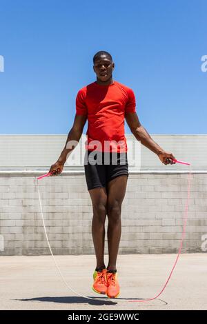 Energetic African American male athlete skipping rope above ground while doing exercises during training in summer Stock Photo