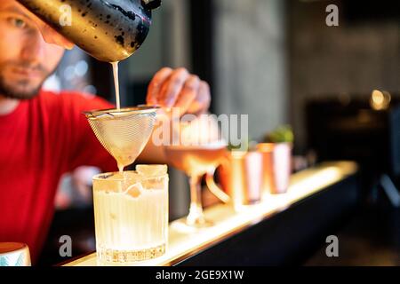 Focused bartender pouring cold refreshing cocktail through strainer in glass placed on counter in bar Stock Photo