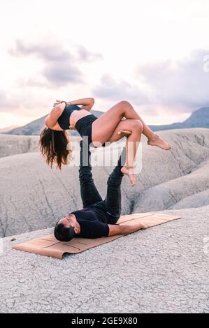 Woman balancing with Namaste hands on legs of man while practicing acroyoga together in highlands Stock Photo
