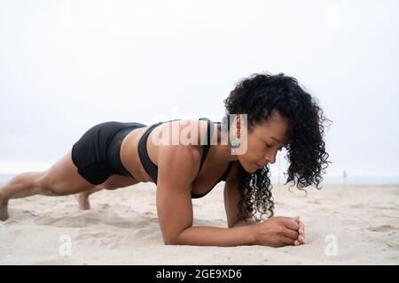 Side view of fit female athlete doing plank exercise while training on sandy shore Stock Photo