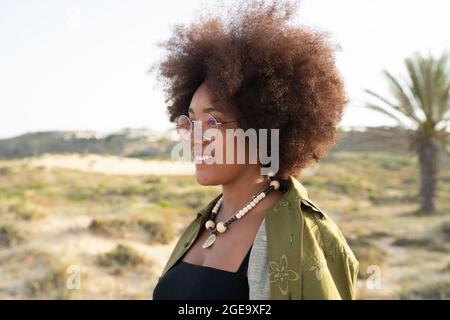 Side view of smiling young African American female with curly hair looking away while enjoying summer holidays in countryside Stock Photo