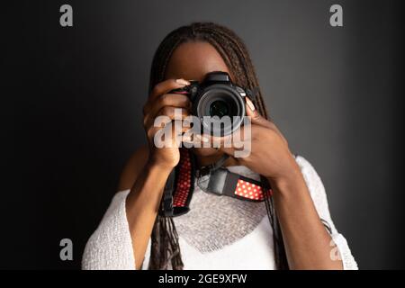 African American female photographer with braids looking through photos taken on professional camera while standing on black background Stock Photo