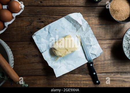Knife ready to cut piece of butter on a pastry preparation on wooden table near eggs and brown sugar Stock Photo